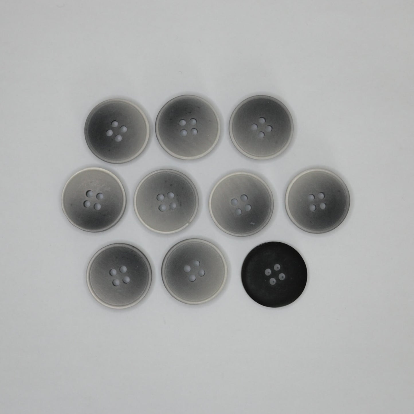 Ten round four-hole buttons arranged in a grid on a plain light background, with eight translucent gray buttons and one solid black button back.