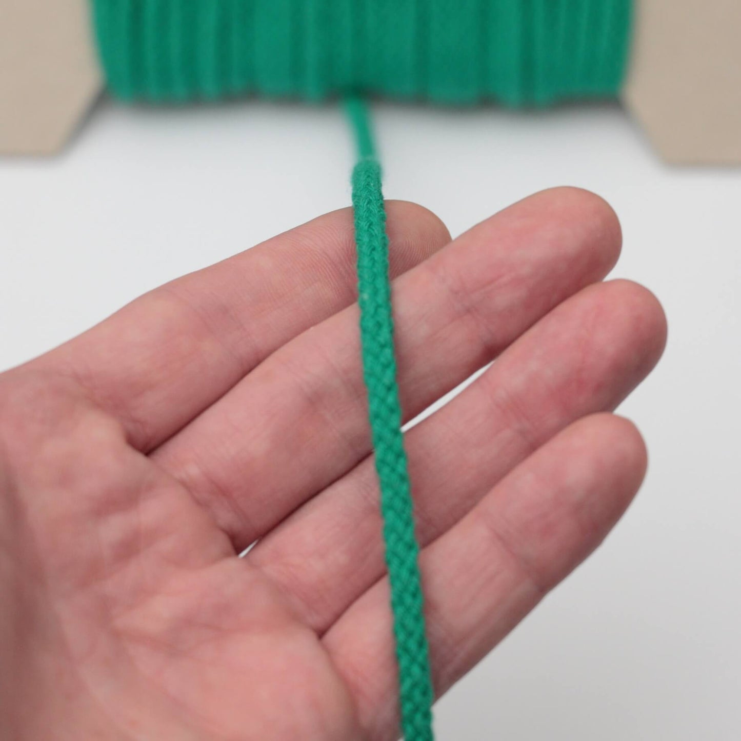 Hand holding a green rope against a white background