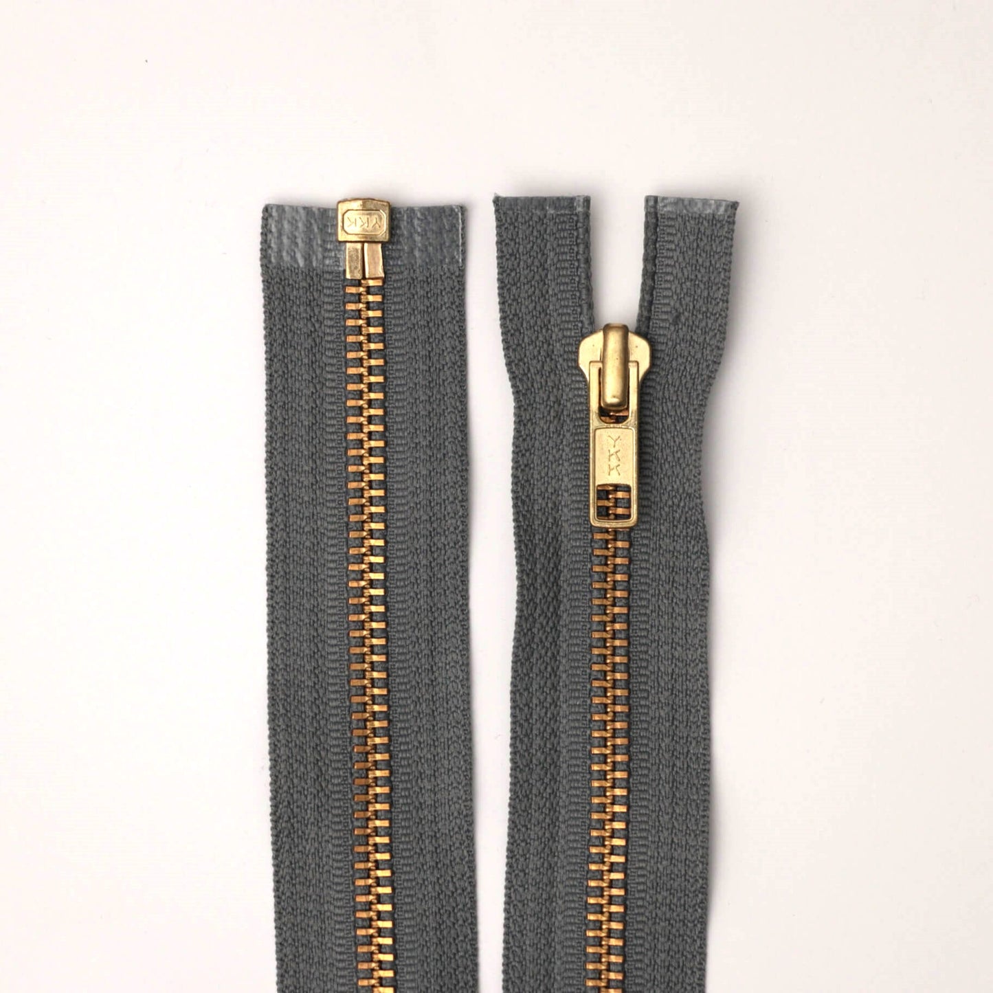 Two gray zippers with gold teeth on a white background