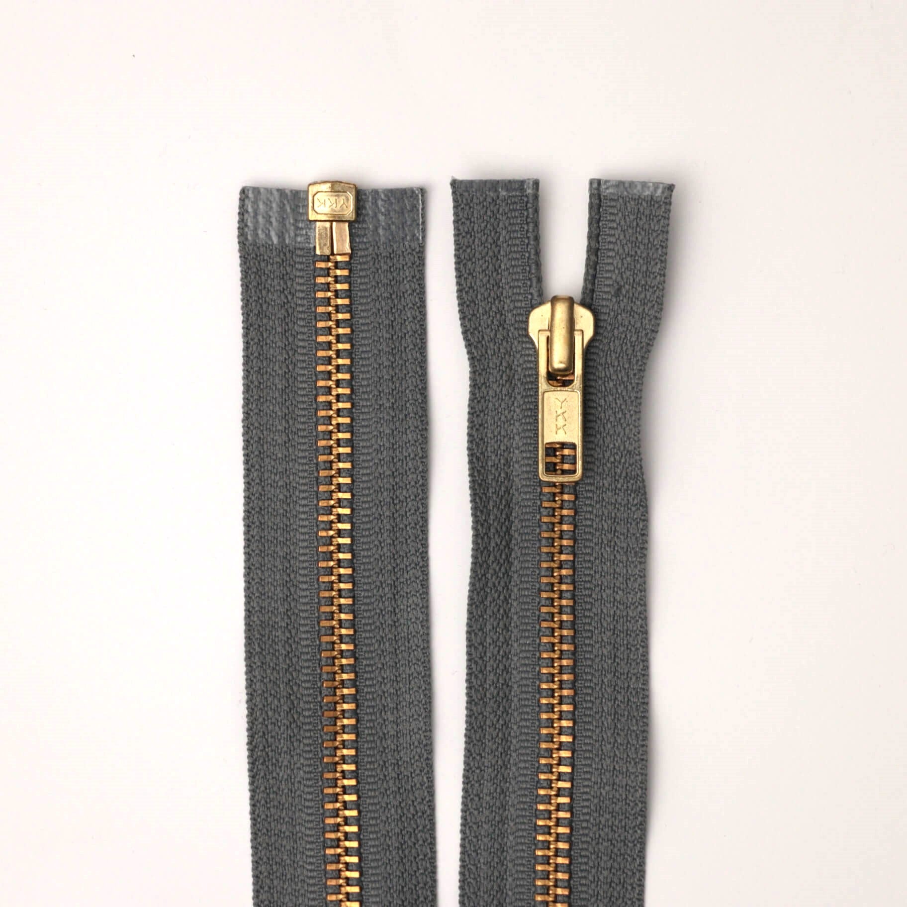 Two gray zippers with gold teeth on a white background