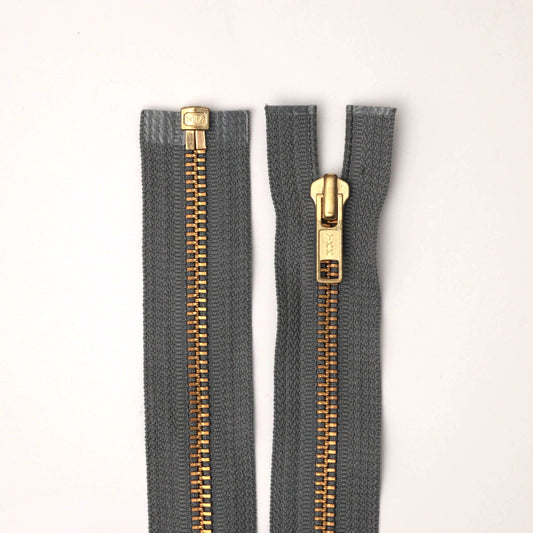 Two gray zippers with gold teeth on a white background