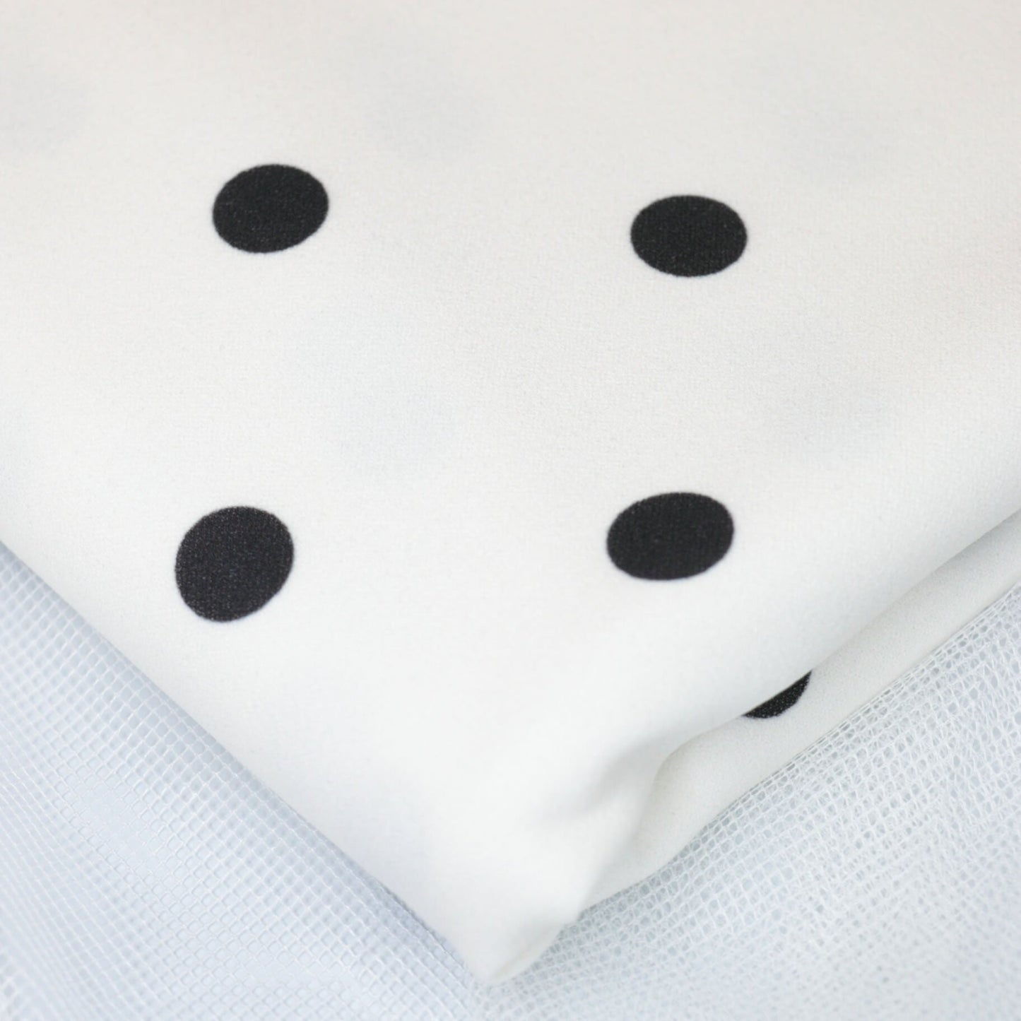 White fabric with black polka dots on a textured white background