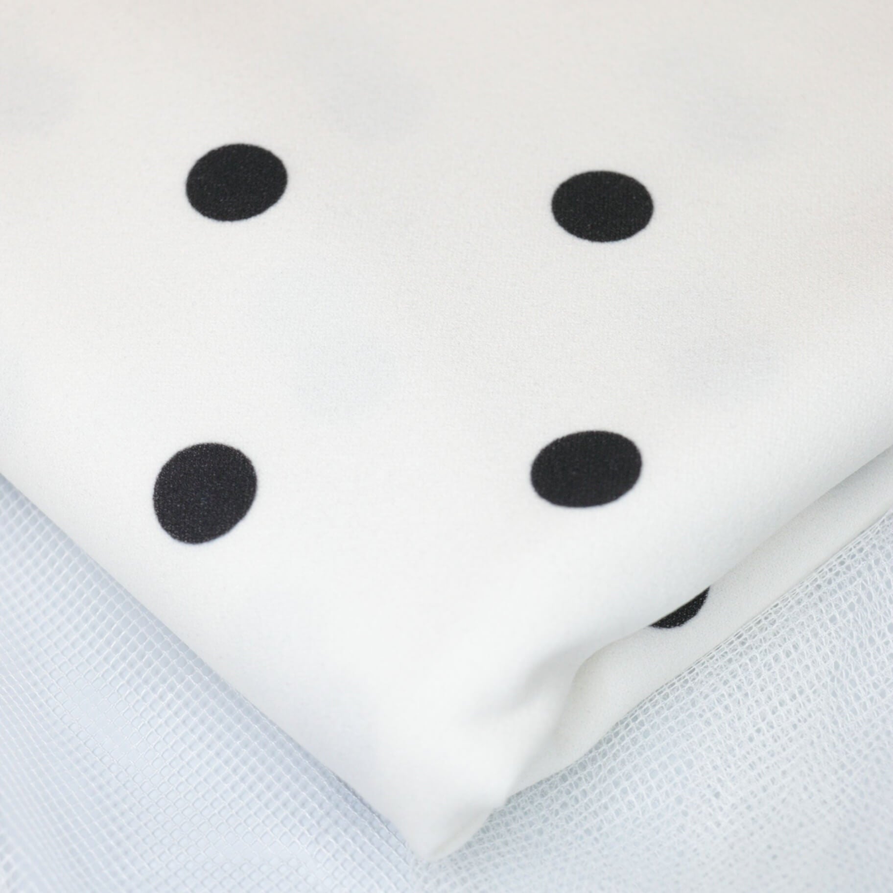 White fabric with black polka dots on a textured white background