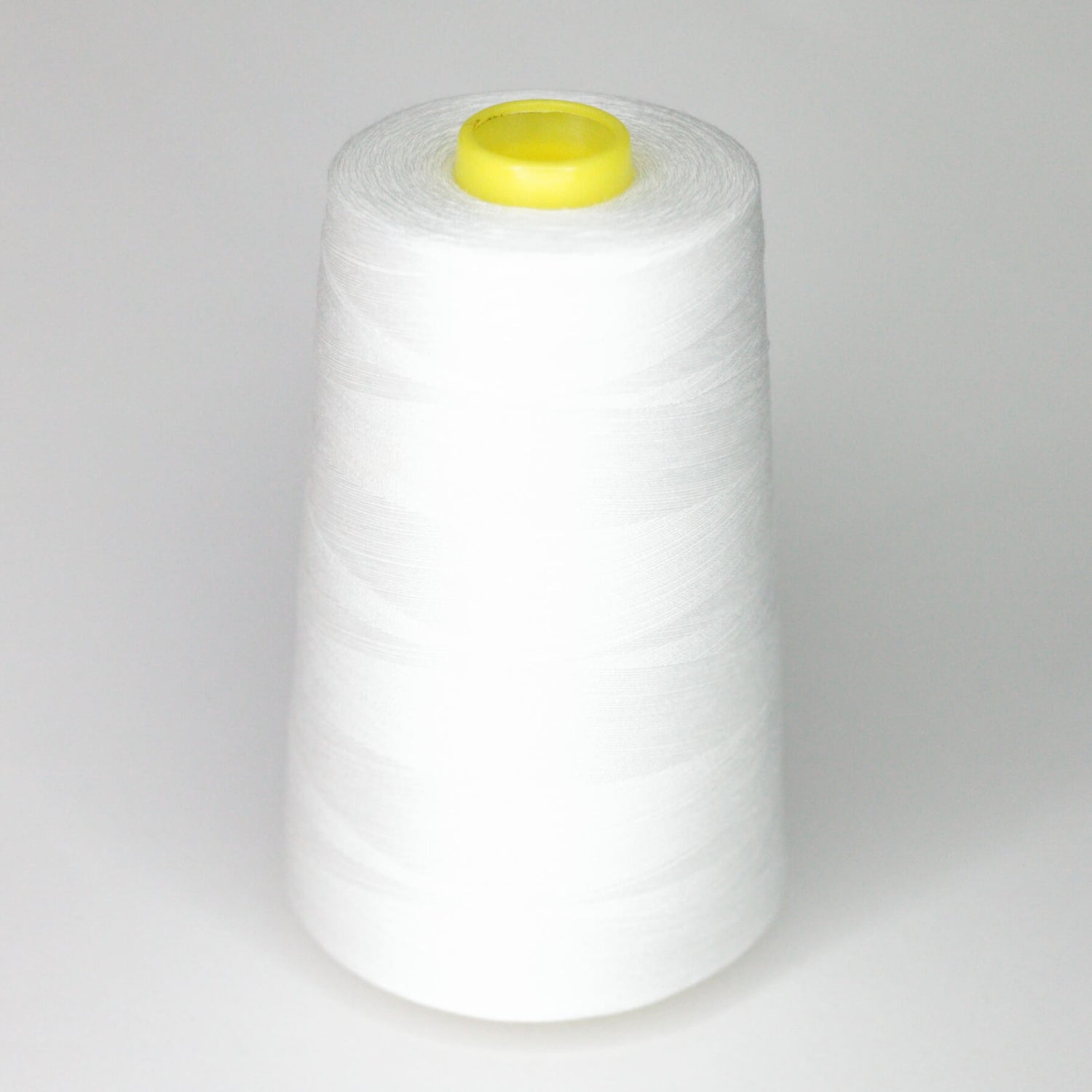 A large spool of raw white 120s cotton sewing thread with a yellow cap on a plain background.